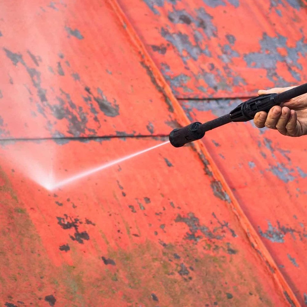 Technician treating embedded rust stains on concrete using controlled pressure washing methods